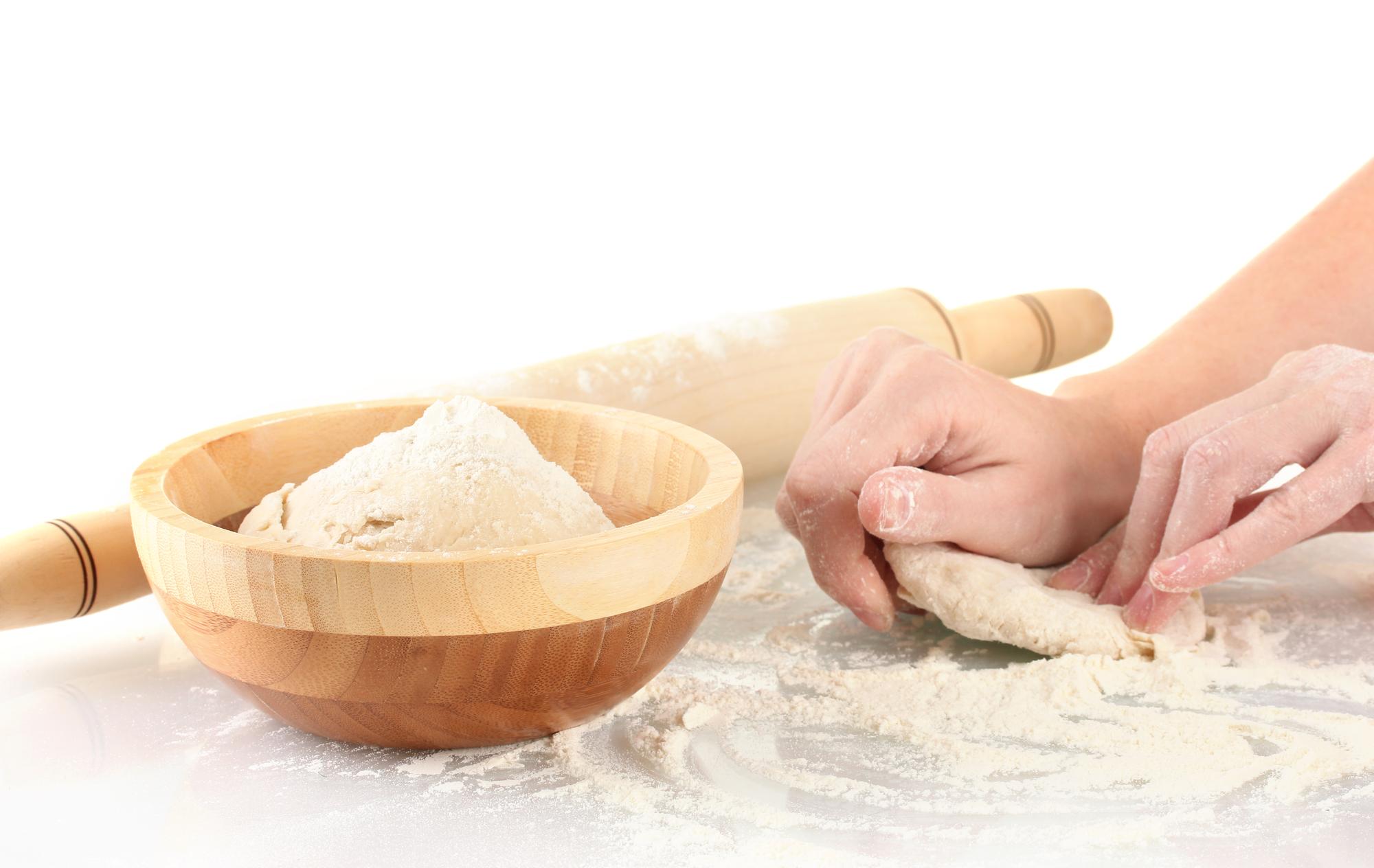 Close-up of hands kneading dough on floured board